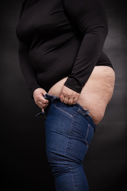 A fat woman puts on small jeans on herself on a black background