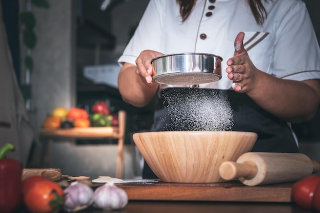 太った女性が台所に立ち、ふるいを使って小麦粉をふるいにかける