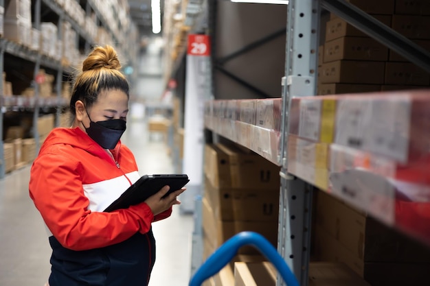 Photo fat woman worker inspecting stock of products while working in large warehouse face mask during coronavirus and flu outbreak virus and illness protection