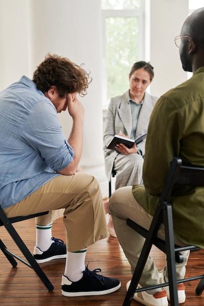Photo fat young man touching head while sitting in front of psychologist at session