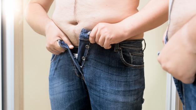 Fat young man trying to fit in small jeans. Concept of male overweight, weight loss and dieting.