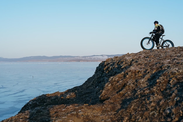 Fatbike（ファットバイクまたはファットタイヤバイクとも呼ばれます）-大きなホイールでのサイクリング。ティーンは、バックグラウンドで雪の山々を自転車で走ります。