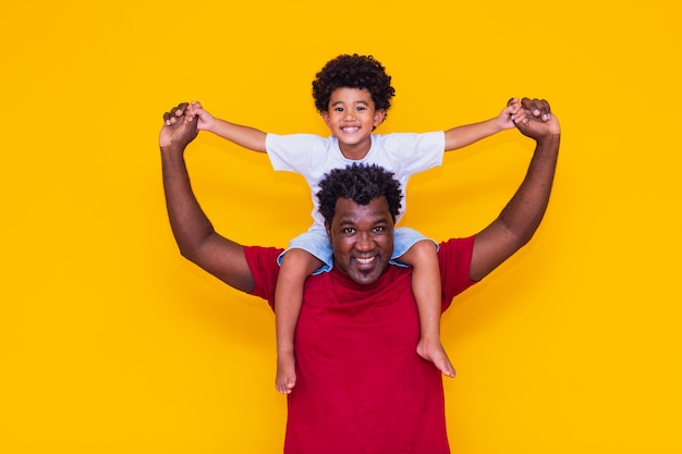 Отец и сын афро на желтом фоне улыбается и играет. Концепция Дня отца