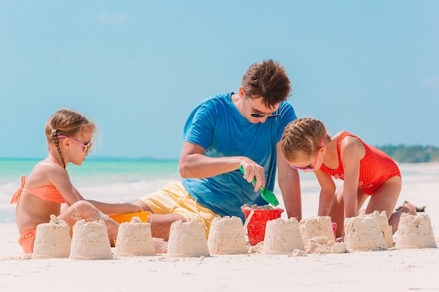 Фото Отец и дети, делая замок из песка на тропическом пляже. семья играет с пляжными игрушками