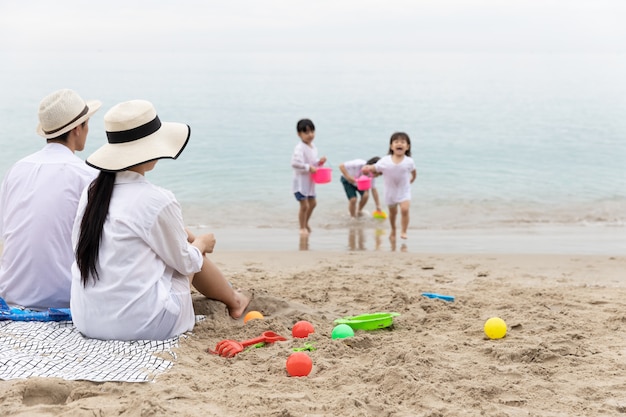 写真 父と母がビーチに座るビーチで砂浜でおもちゃを一緒に遊んでいる子供たちを見る。休日と旅行のコンセプトです。