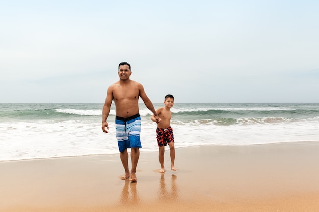 写真 父と息子の夏のショートパンツ、旅行、家族での休暇の概念でビーチの上を歩く