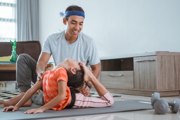 Father assisting his daughter to do stretching at home. kid exercising with parent doing gymnastic