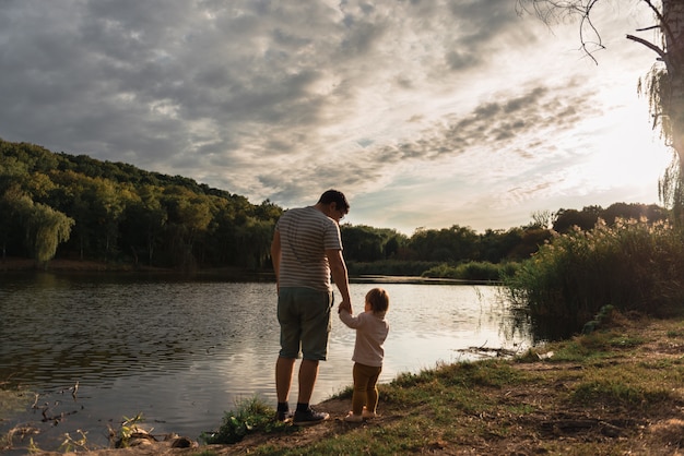 Father and baby girl sitting near lake. Local travel. New normal vacation. Father's day