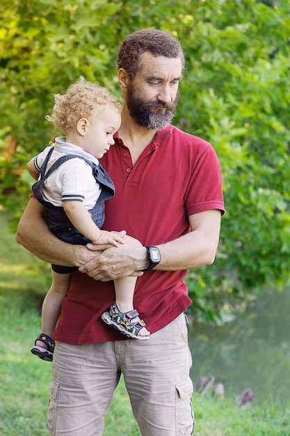 Photo father carrying cute son while standing outdoors