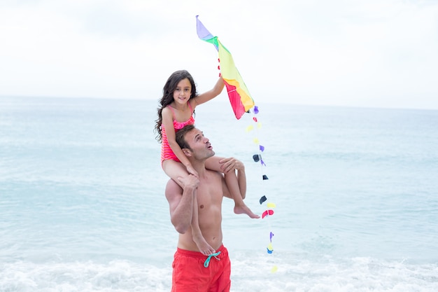 Father carrying daughter with kite at beach