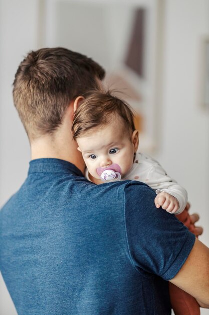 Foto padre che porta una piccola bambina con il succhietto in braccio