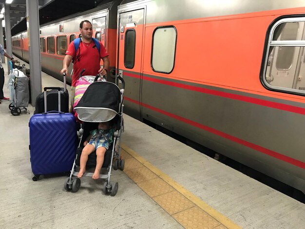 鉄道 駅 の プラットフォーム で 赤ちゃん の 車輪 で 息子 を 背負っ て いる 父