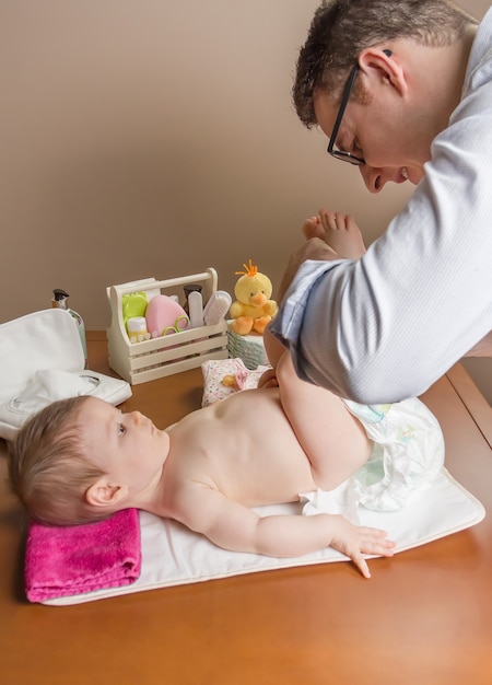 Father changing diaper of adorable baby with a hygiene set for babies on the background