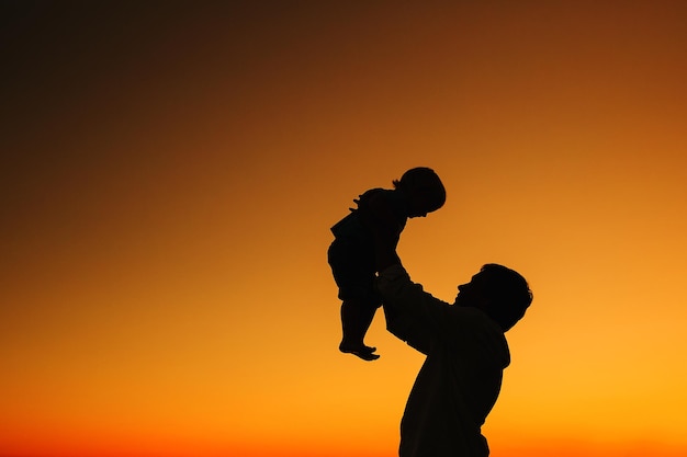 Father and child son silhouettes at sunset sky Loving family and summer vacation Man and kid boy playing together outdoors on a sea beach