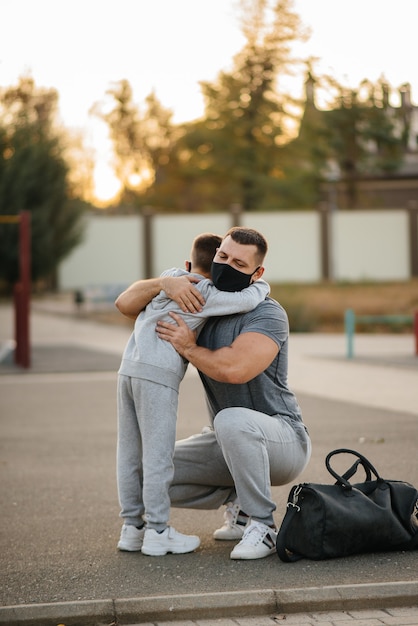 Отец и ребенок стоят на спортивной площадке в масках после тренировки во время заката