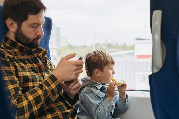 Father and child travelling by train Man using smartphone boy eating apple