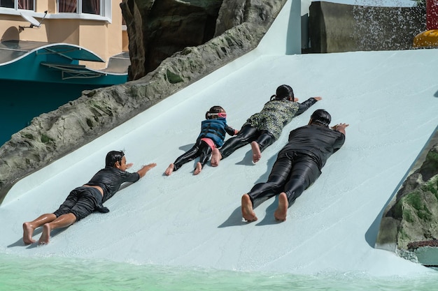 Father and children sliding into pool after going down water slide during summer