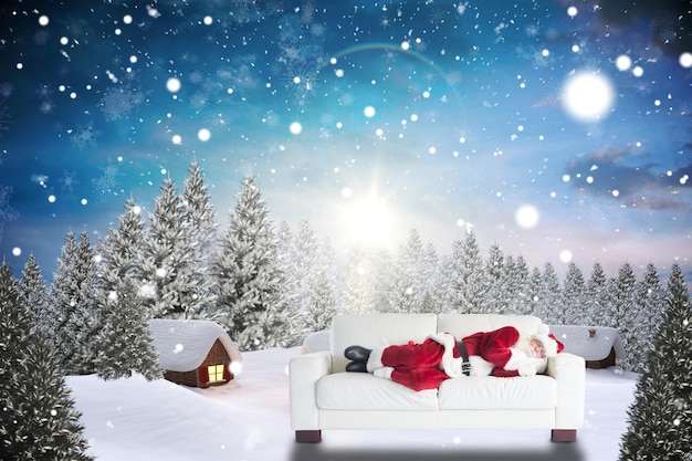 Photo father christmas sleeps on a couch against snow covered village in forest