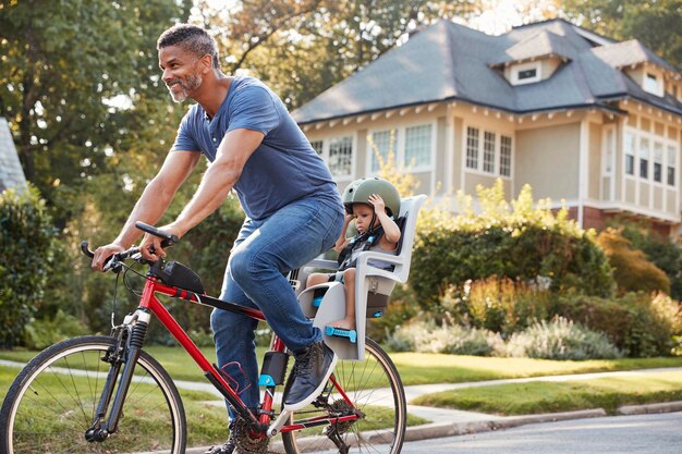 Father Cycling Along Street With Daughter In Child Seat