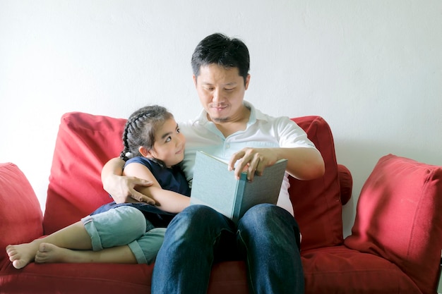 아버지와 딸이 책을 읽고 있습니다빨간 소파에 앉아 좋은 학습 습관과 좋은 가족 관계입니다
