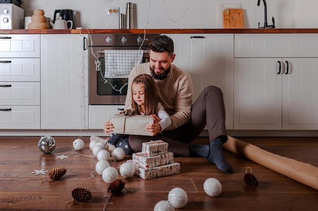 Father and daughter decorate christmas gifts at home. Family opens christmas toys on wooden floor.