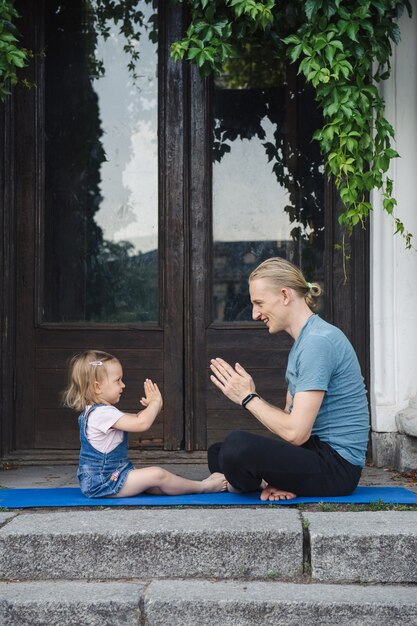 Father and daughter doing yoga together outdoor in the park near the old building. Happy family spends time together. Healthy lifestyle concept.