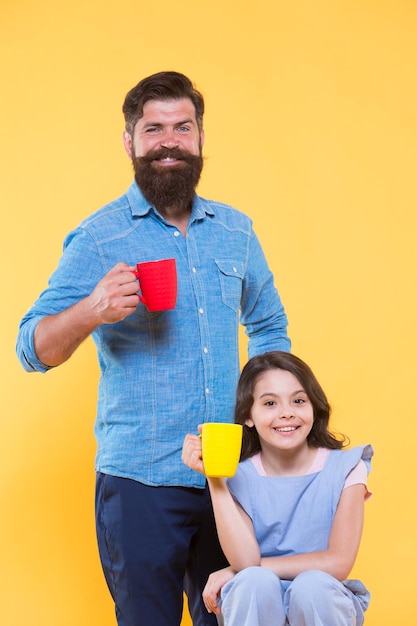 Father and daughter drink tea at home Tea party concept Good morning Having coffee together Water balance and health care Family drinking tea Bearded man and happy little girl holding mugs