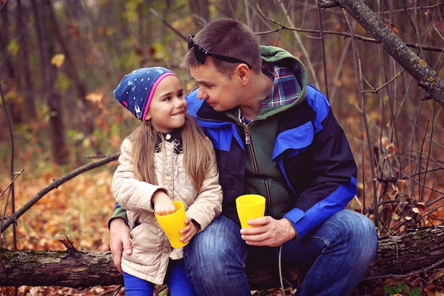 Father and daughter drinking tea in the autumn forest