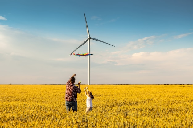 Father and daughter having fun, playing with kite together on the Wheat Field on Bright Summer day