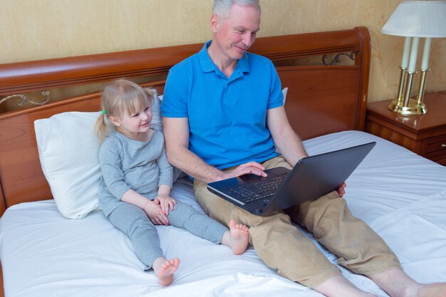 Father and daughter laying on bed and using laptop at home,