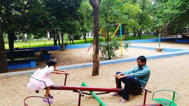 Photo father and daughter playing on seesaw at park