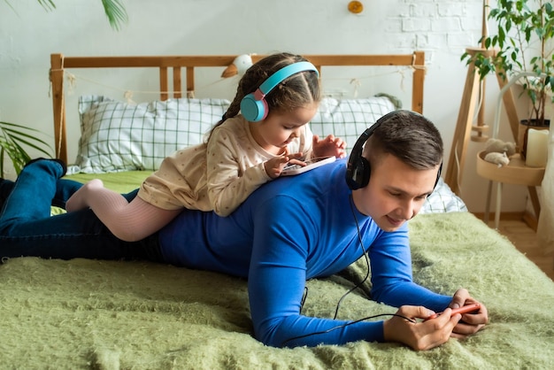 Father and daughter playing on smartphone together wearing headphones at home Good parent and child relations