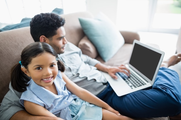 Father and daughter sitting on sofa and using laptop