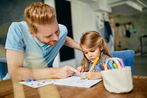 Father and daughter sitting at table painting colouring book