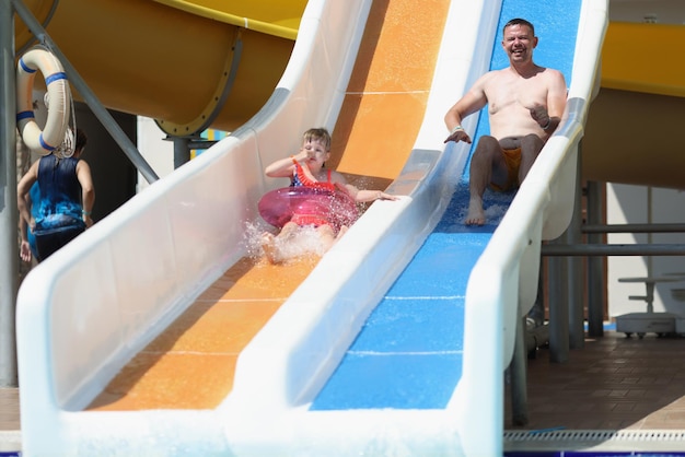 Father and daughter slide down hill on air mattress in water park