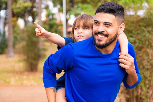 Father and daughter smiling at camera in the park Daughter climbs on daddy's back Happy Fathers Day