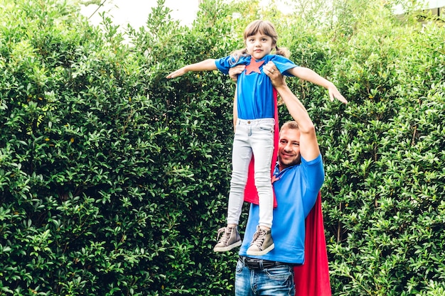 Photo father and daughter in superhero costume playing against plants