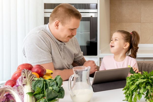 Father And Daughter Using Digital Tablet In Kitchen At Home