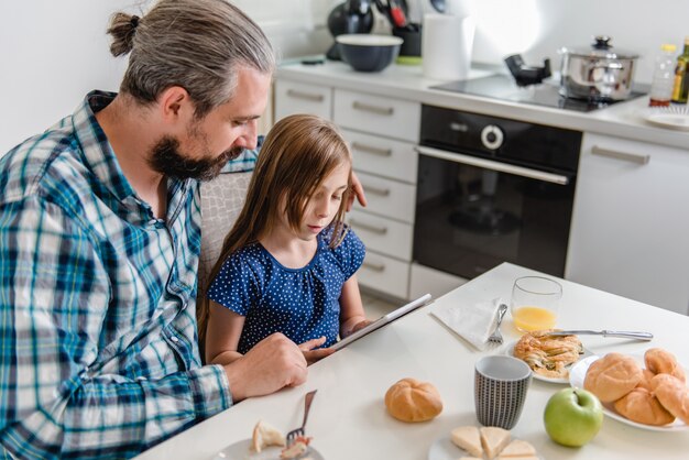 父と娘が朝食時にタブレットを使用して