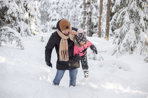 父と娘が歩いて、冬の雪の森で楽しんでいます