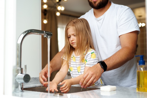 Padre e figlia che si lavano le mani sopra il lavandino in una cucina