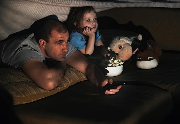 Father and daughter watching a movie at home on the couch