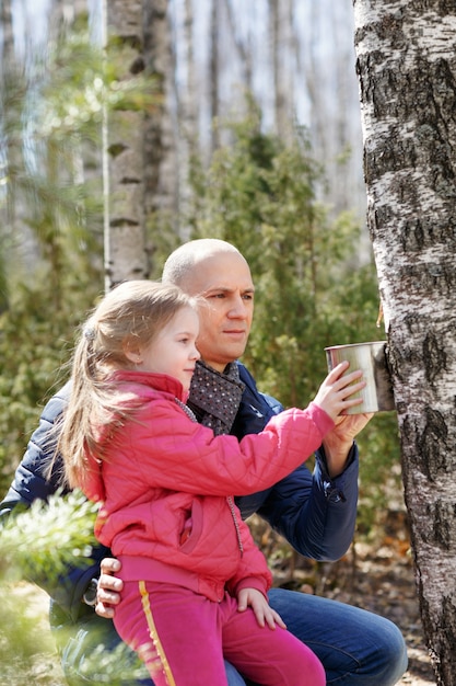 Photo father and daughter in the woods collect birch sap