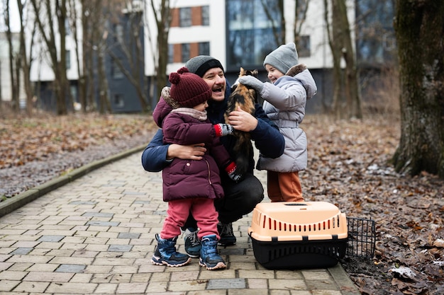 Father and daughters with cat in travel pet plastic cage carriage outdoor at park