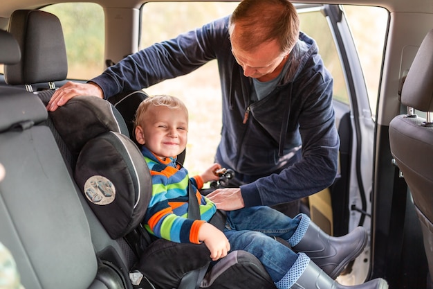 Father fastening safety belt for his baby boy in his car seat.