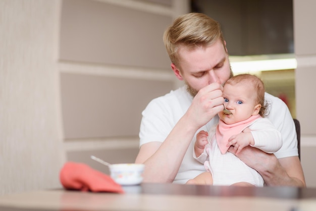 Father feeding his daughter fruit puree in the kitchen