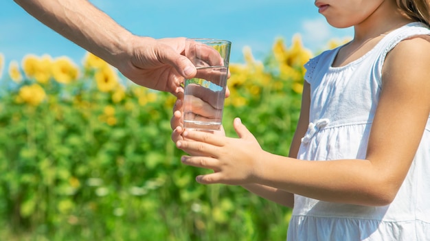 The father gives the child water in the background of the field