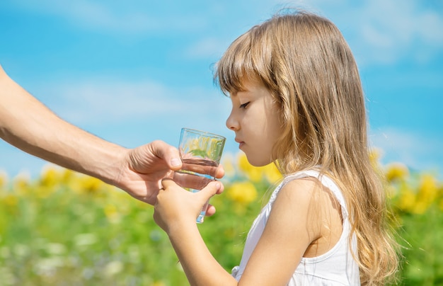 The father gives the child water in the background of the field