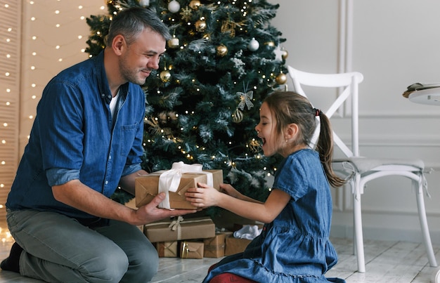 A father gives his daughter a gift in the room of a festively decorated house. happy christmas