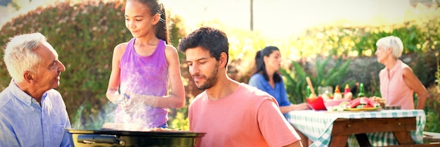 Padre e nonno guardano mentre la ragazza prepara il barbecue